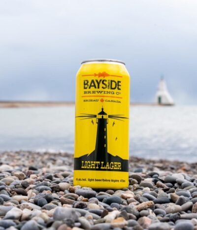 A yellow can of Lighthouse Light Lager on a rocky beach.