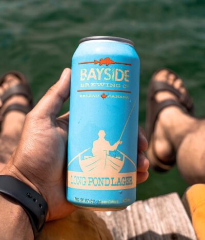 A blue can of Long Pond Lager held over a lake.