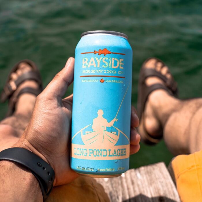 A blue can of Long Pond Lager held over a lake.